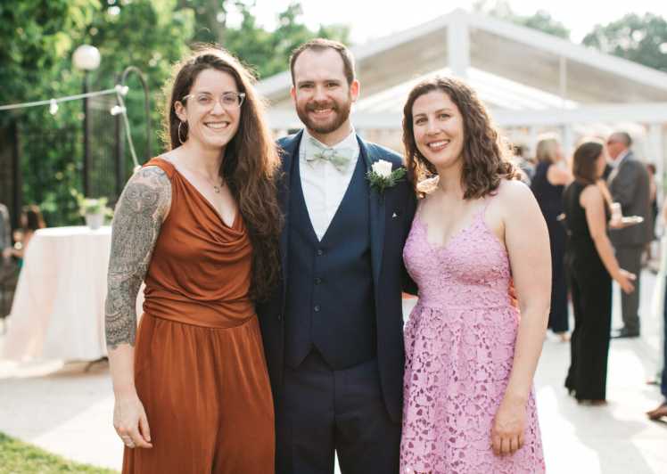 two females smiling with an arm around a male in the center wearing dress clothes
