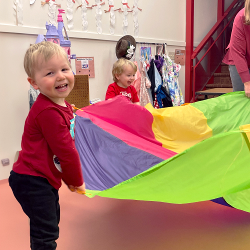 Preschool children playing with a large, colorful parachute as part of an exercise activity to promote healthy habits.