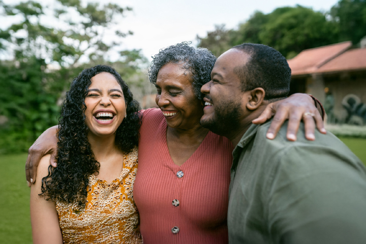 Three family members joyfully laughing and smiling in a grassy area, capturing a moment of happiness outdoors.