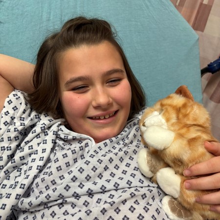 Girl smiling while wearing hospital gown and holding stuffed plush cat