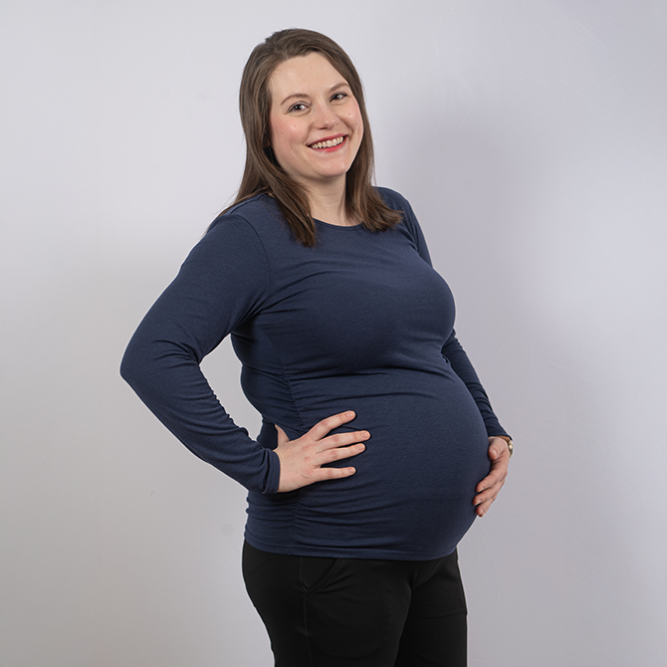 Pregnant woman in dark blue shirt smiling and holding her belly