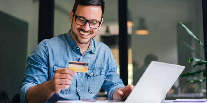 man smiling with credit card and laptop in front of him