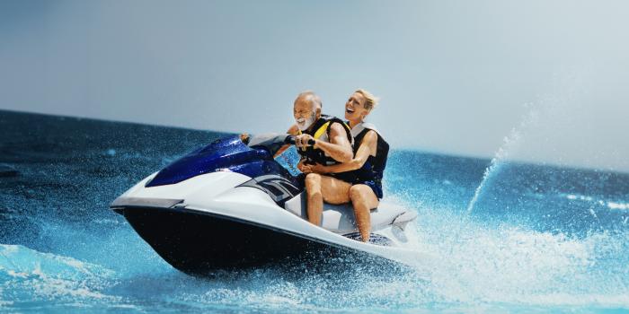 A senior couple rides jetski in the ocean after joint replacement. 