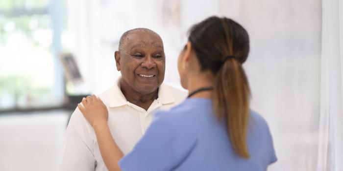 Senior male patient smiling with female provider's hand on his shoulder
