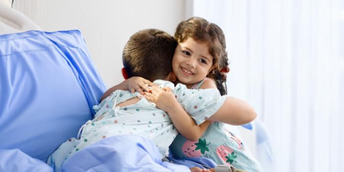 Two young siblings hug in a hospital bed